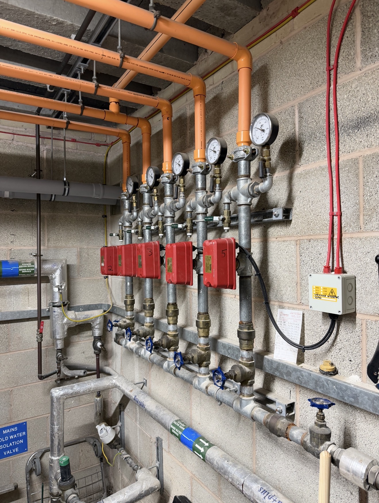 Sprinkler control valves and pressure gauges connected to orange CPVC pipework in a plant room